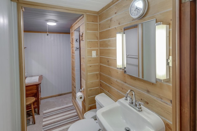 half bathroom featuring baseboards, a sink, wooden walls, and toilet