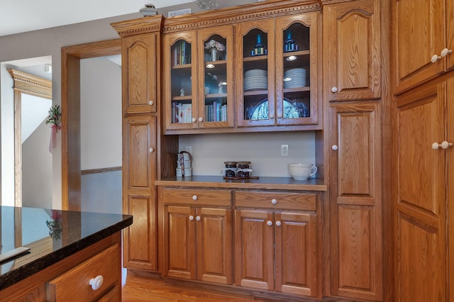 617 17th St N, Sartell, MN 56377 - kitchen featuring brown cabinetry, glass insert cabinets, light wood finished floors, and dark stone countertops