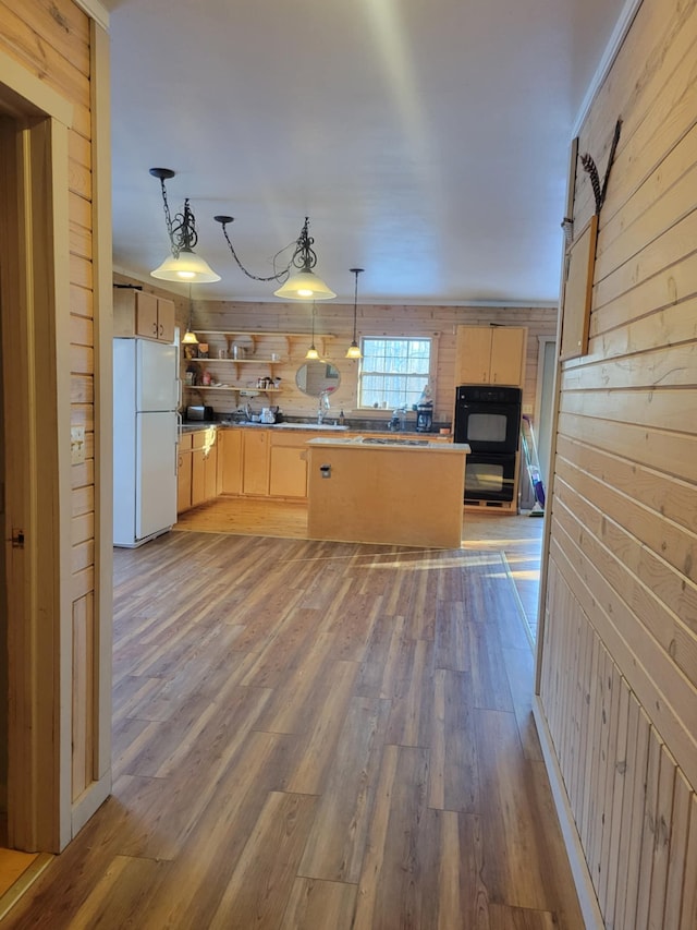 kitchen featuring light brown cabinetry, a sink, freestanding refrigerator, and wooden walls