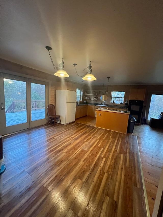 kitchen with freestanding refrigerator, hanging light fixtures, and wood finished floors