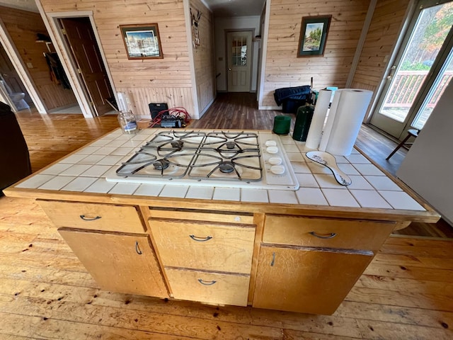 kitchen featuring tile countertops, white gas stovetop, wood walls, and wood finished floors