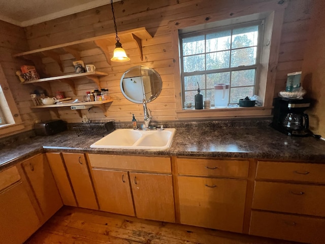 kitchen with pendant lighting, dark countertops, a sink, and wooden walls