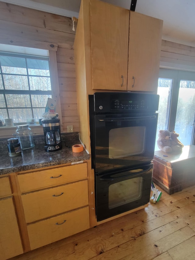 kitchen featuring light wood finished floors, wood walls, dark stone countertops, and dobule oven black