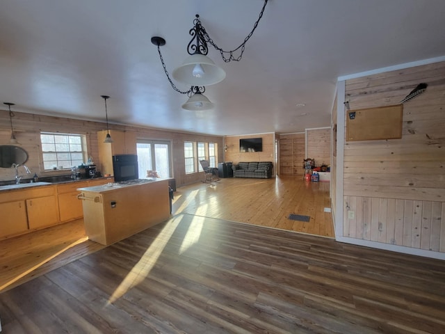 kitchen featuring light brown cabinets, wood walls, a kitchen island, a sink, and wood finished floors