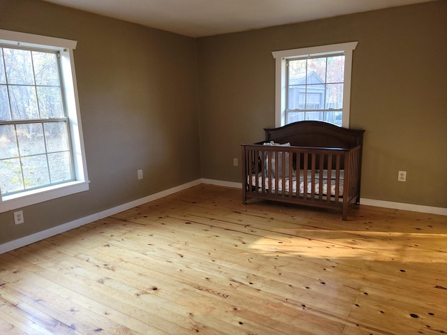 unfurnished bedroom with hardwood / wood-style floors, multiple windows, a crib, and baseboards