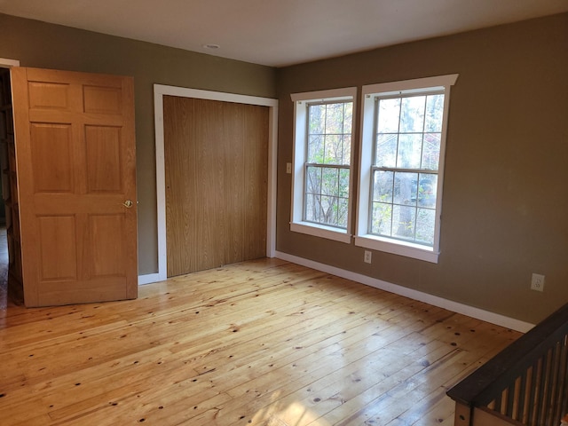 unfurnished bedroom with a closet, wood-type flooring, multiple windows, and baseboards