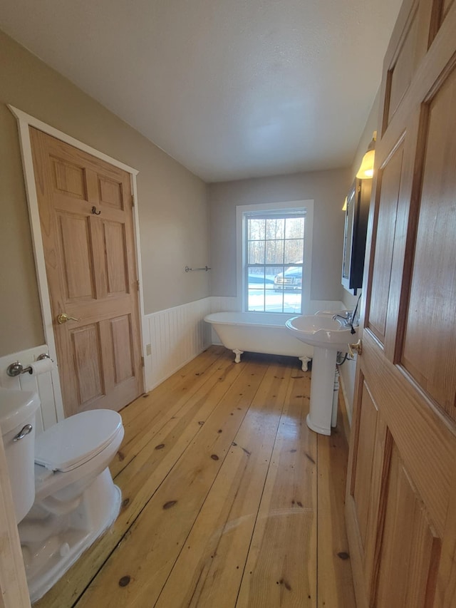 full bath with toilet, a wainscoted wall, hardwood / wood-style flooring, a soaking tub, and a sink