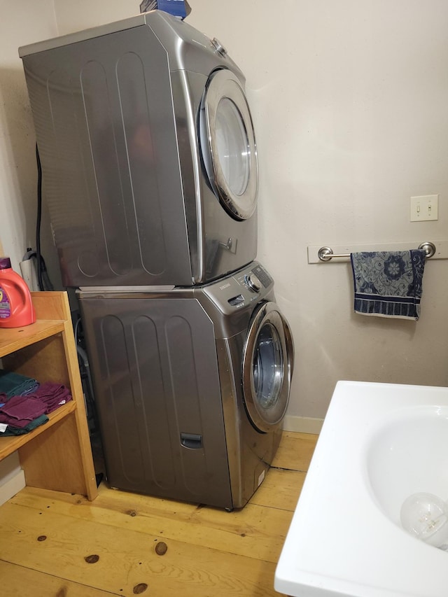 clothes washing area featuring a sink, light wood-style floors, baseboards, and stacked washer / drying machine