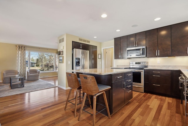 kitchen with stainless steel appliances, a breakfast bar area, a kitchen island, and light wood-style flooring