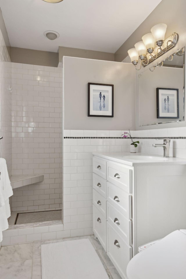 full bathroom with toilet, marble finish floor, a tile shower, vanity, and tile walls