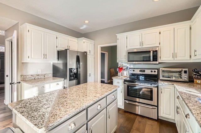 kitchen featuring light stone counters, a toaster, stainless steel appliances, a center island, and dark wood-style floors