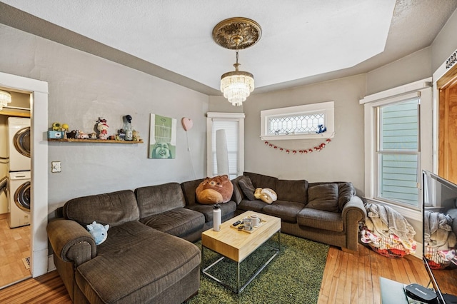 living room with stacked washer / drying machine, a notable chandelier, and hardwood / wood-style flooring