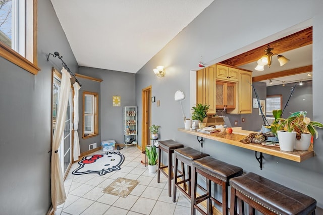 kitchen featuring light tile patterned floors, visible vents, light brown cabinets, a kitchen breakfast bar, and baseboards