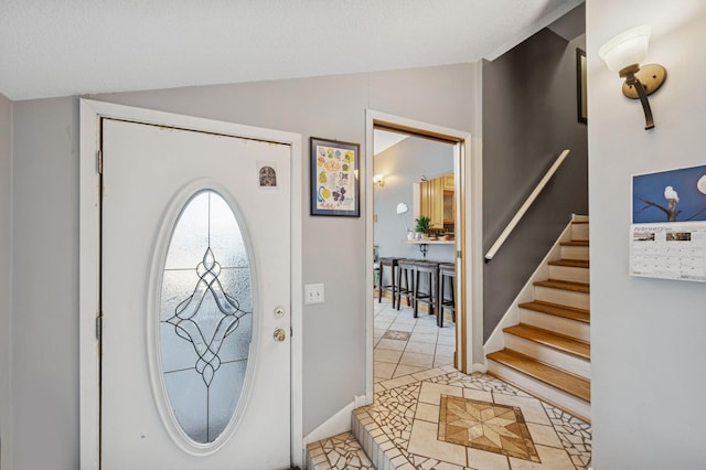 entryway with stairs, lofted ceiling, baseboards, and light tile patterned floors