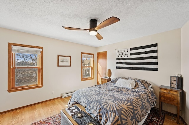 bedroom with a textured ceiling, multiple windows, wood finished floors, and baseboards