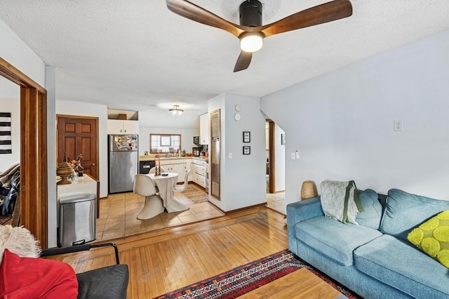 living room with a textured ceiling, light wood-style flooring, and a ceiling fan