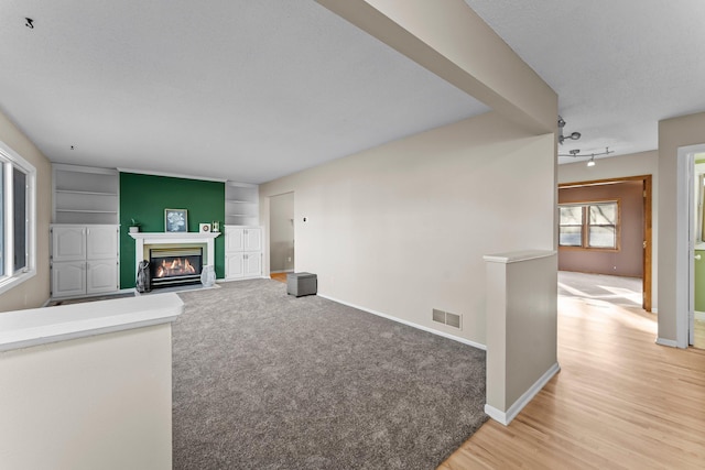 living room featuring a fireplace with flush hearth, visible vents, baseboards, and light colored carpet