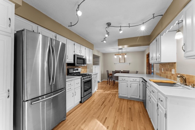 kitchen with light wood finished floors, appliances with stainless steel finishes, white cabinetry, a sink, and a peninsula