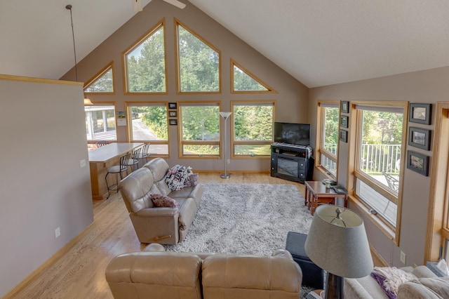 living area featuring light wood-style floors, baseboards, high vaulted ceiling, and a wealth of natural light