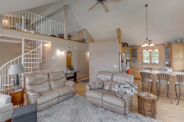 living area featuring high vaulted ceiling, light wood-type flooring, ceiling fan, and stairway