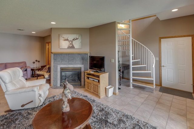 living area with light tile patterned floors, recessed lighting, a tiled fireplace, baseboards, and stairs