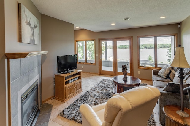 living area with a tile fireplace, visible vents, plenty of natural light, and a textured ceiling