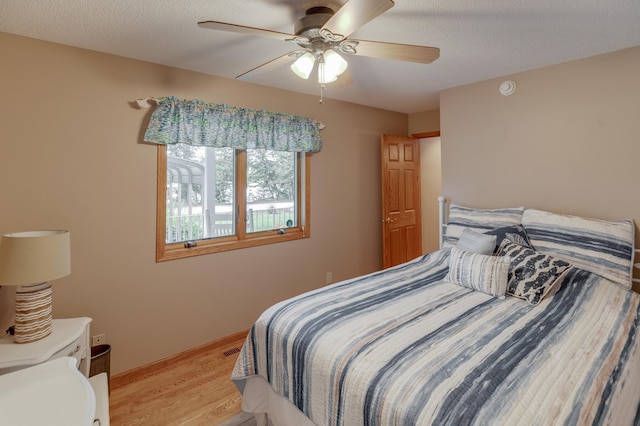 bedroom with a textured ceiling, light wood finished floors, visible vents, and a ceiling fan