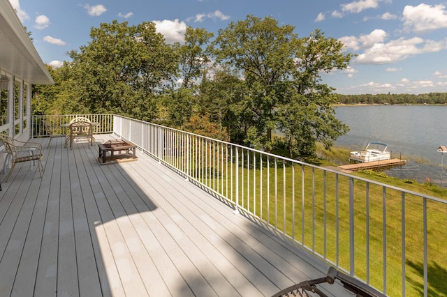 wooden deck with a water view, an outdoor fire pit, and a yard