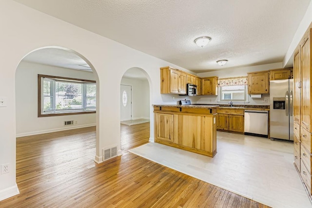 11570 Juniper St NW, Coon Rapids, MN 55448 - kitchen with stainless steel appliances, a textured ceiling, light wood-type flooring, arched walkways, and plenty of natural light