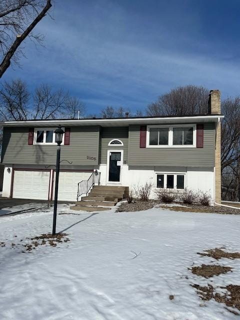 raised ranch with a garage, driveway, and a chimney