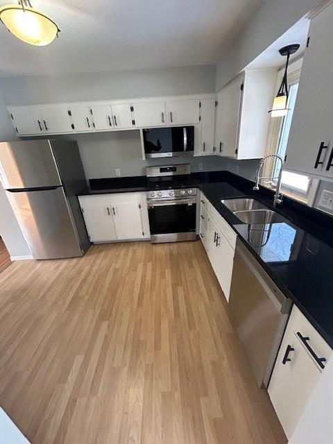 kitchen featuring a sink, stainless steel appliances, dark countertops, and light wood finished floors