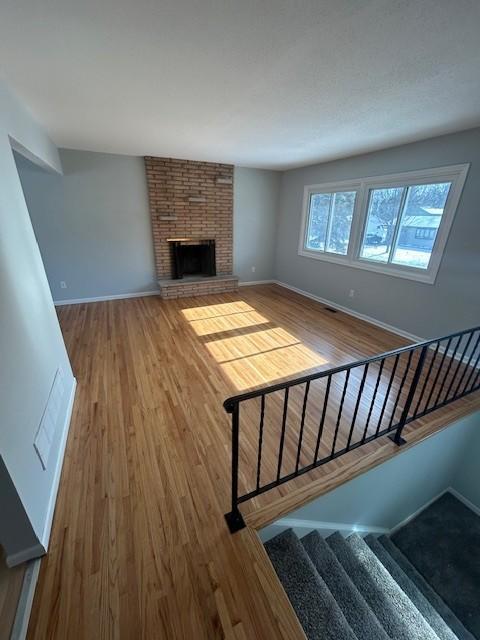 unfurnished living room with visible vents, a brick fireplace, baseboards, stairs, and wood finished floors