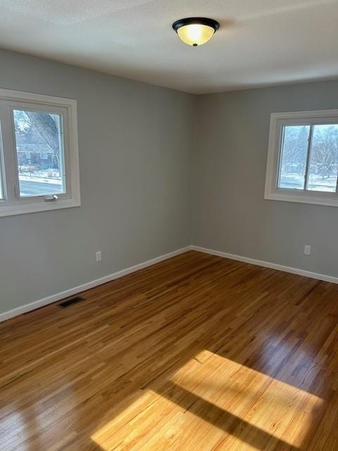 unfurnished room with wood finished floors, visible vents, and baseboards