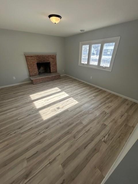 unfurnished living room with baseboards, a brick fireplace, and wood finished floors