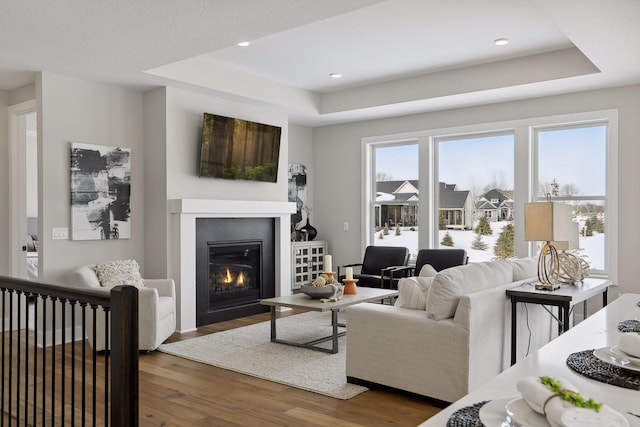 living area with a tray ceiling, dark wood-style flooring, a glass covered fireplace, and recessed lighting