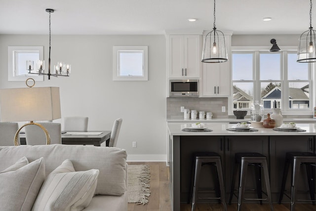 kitchen featuring a kitchen breakfast bar, light countertops, stainless steel microwave, and white cabinets