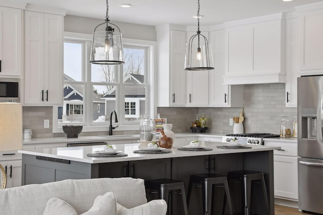 kitchen with a center island, stainless steel appliances, light countertops, white cabinetry, and a kitchen bar