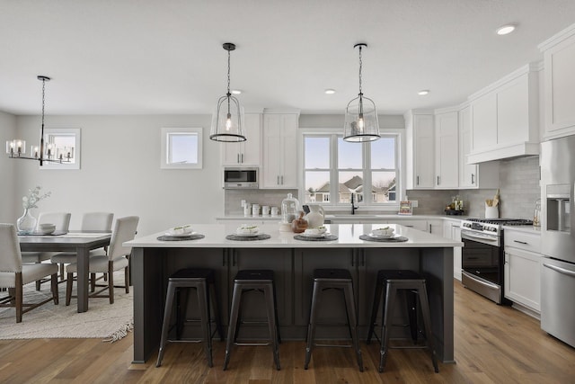 kitchen featuring stainless steel appliances, a kitchen island, white cabinets, light countertops, and a kitchen bar