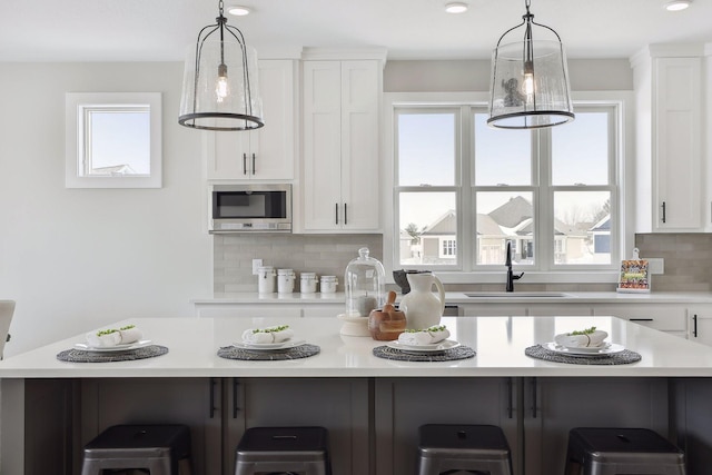 kitchen with white cabinets, a spacious island, stainless steel microwave, light countertops, and a sink