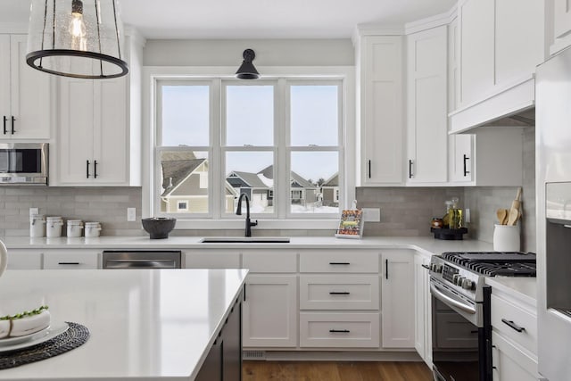 kitchen with decorative light fixtures, light countertops, appliances with stainless steel finishes, white cabinetry, and a sink