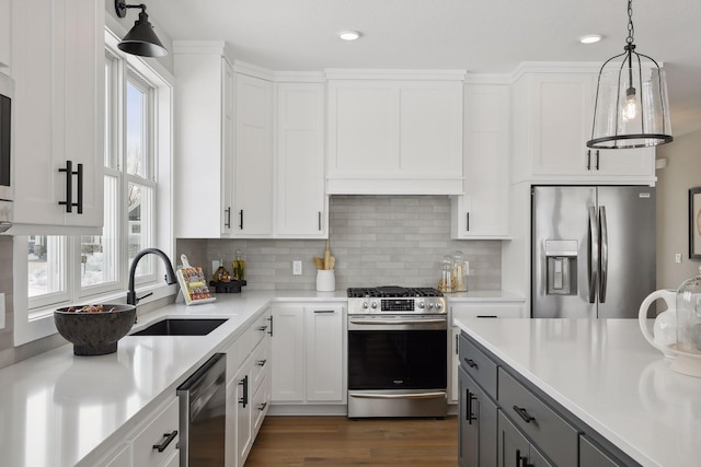 kitchen with stainless steel appliances, a sink, white cabinets, hanging light fixtures, and light countertops