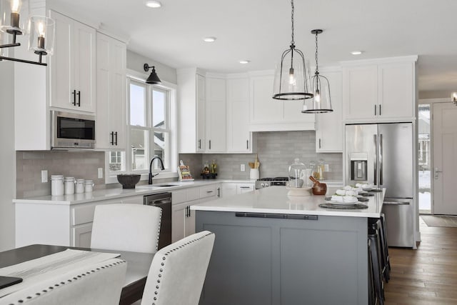 kitchen with stainless steel appliances, white cabinets, light countertops, hanging light fixtures, and a center island