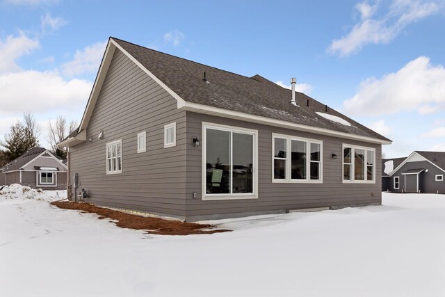 snow covered back of property with a shingled roof