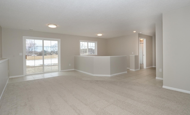 empty room with light colored carpet, a textured ceiling, baseboards, and light tile patterned floors