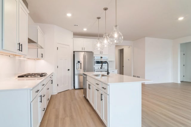 kitchen with light countertops, appliances with stainless steel finishes, white cabinets, a kitchen island with sink, and a sink