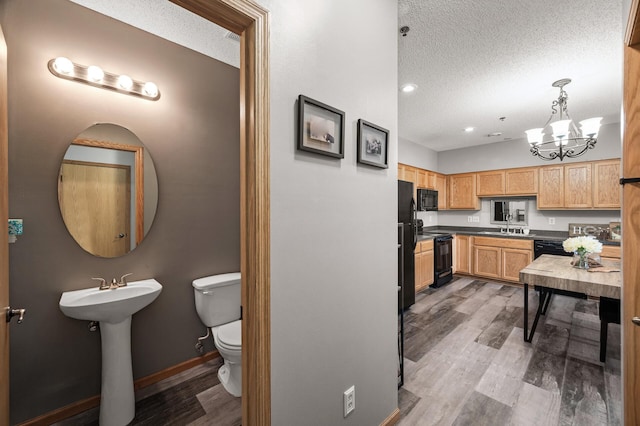 interior space featuring a textured ceiling, light brown cabinets, wood finished floors, baseboards, and black appliances