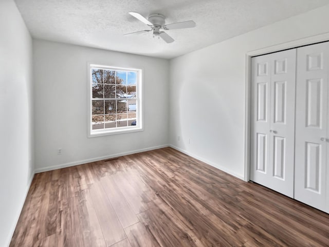 unfurnished bedroom featuring a closet, a textured ceiling, baseboards, and wood finished floors