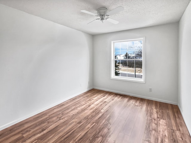 spare room with a textured ceiling, wood finished floors, a ceiling fan, and baseboards