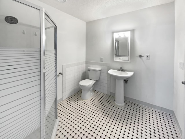 full bathroom featuring toilet, a sink, a textured ceiling, a shower stall, and tile walls