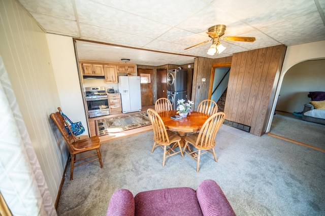 dining space featuring light carpet, wooden walls, ceiling fan, arched walkways, and a drop ceiling